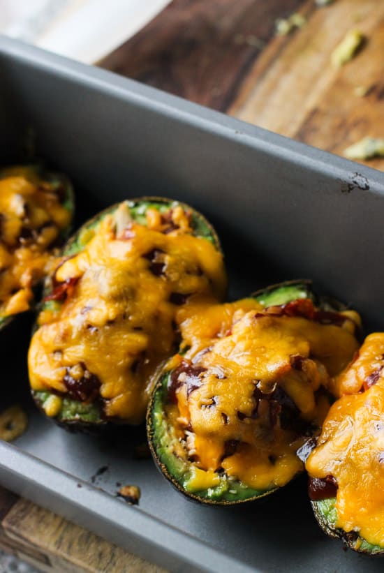 Baked and stuffed avocado boats lined up in a metal loaf pan.