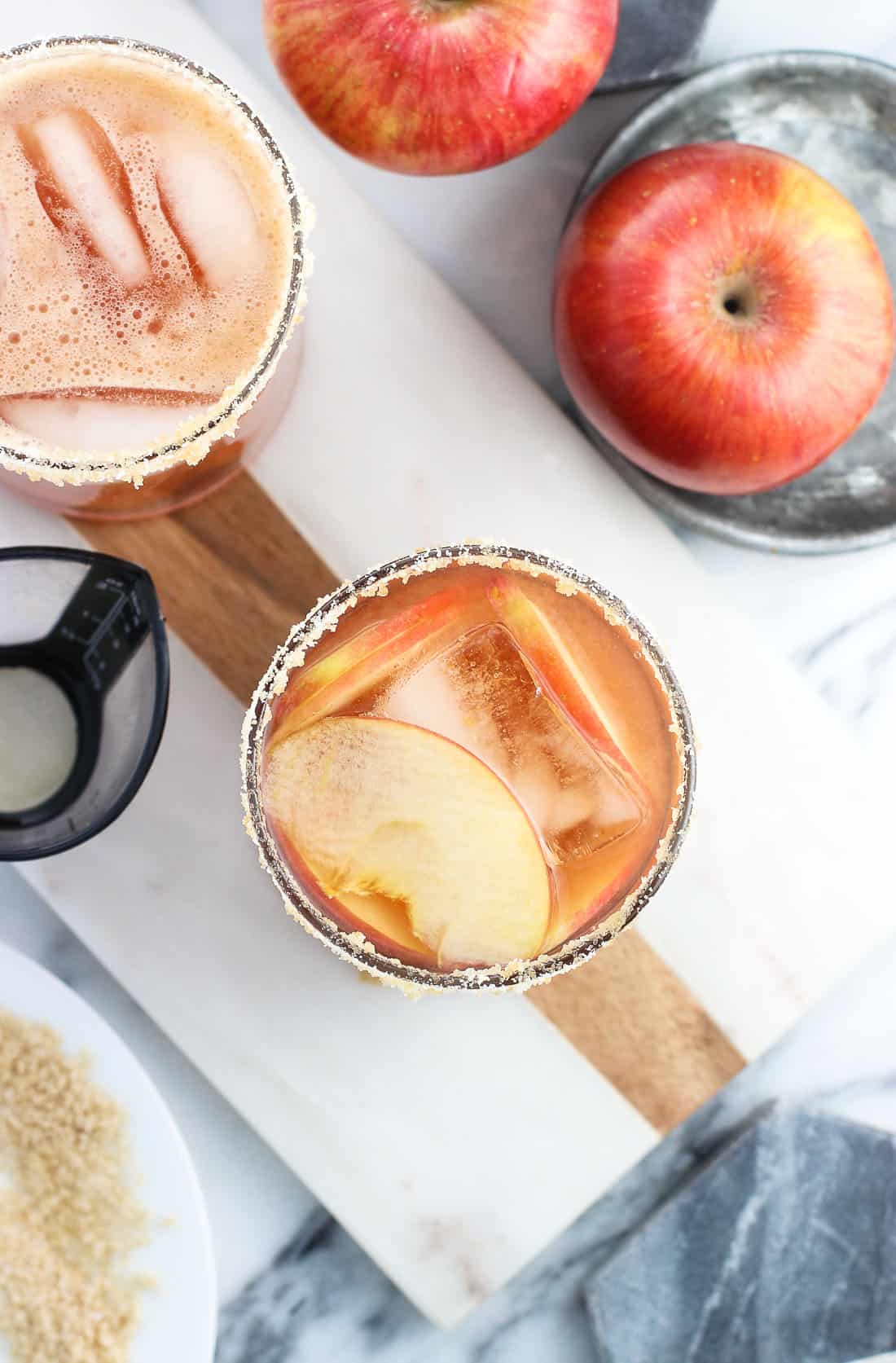 Two cranberry apple margaritas garnished with thin apple slices on a marble board.