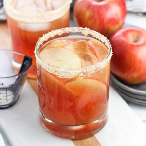 Two cranberry apple margaritas with sugared rims next to apples.