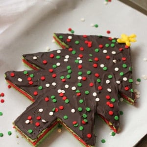 A Christmas tree-shaped and decorated slab of rainbow cookies on a parchment-lined baking sheet.