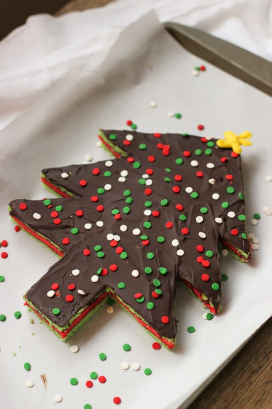 A Christmas tree-shaped and decorated slab of rainbow cookies on a parchment-lined baking sheet.