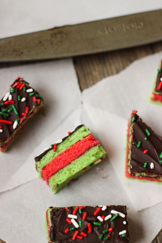 Various shaped Christmas rainbow cookies on sheets of parchment paper.