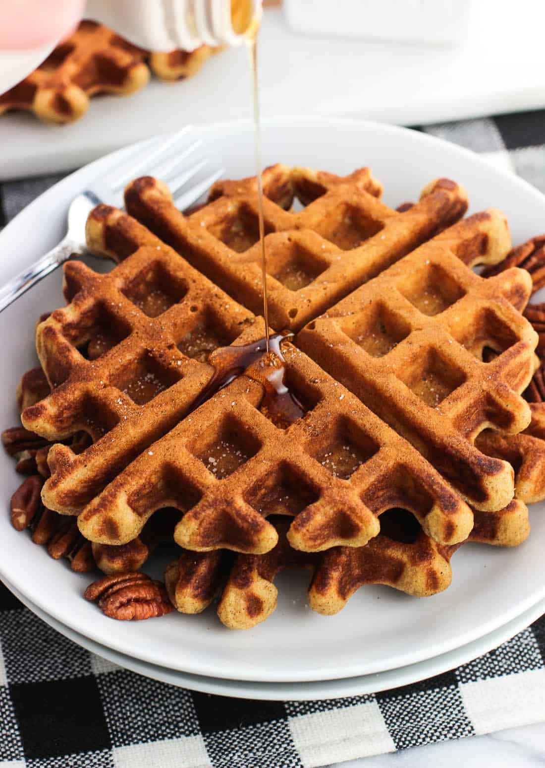 Two waffles on a plate being drizzled by maple syrup