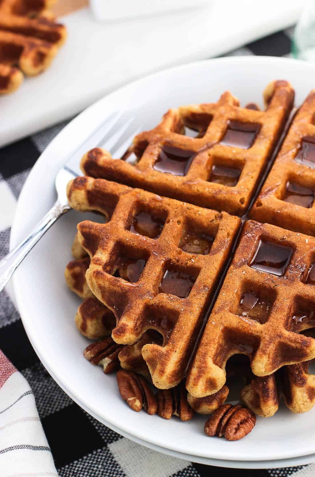 Two waffles on a plate served with maple syrup and pecans