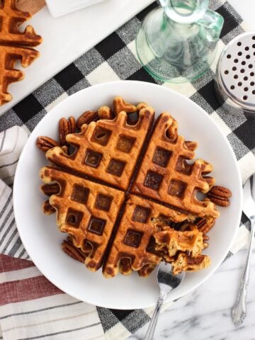 An overhead shot of waffles on a plate served with maple syrup and pecans