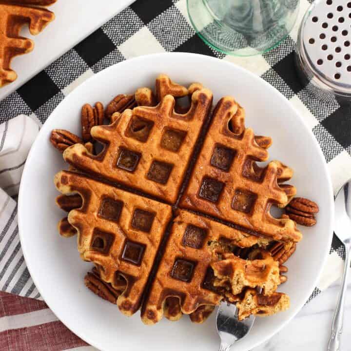 An overhead shot of waffles on a plate served with maple syrup and pecans