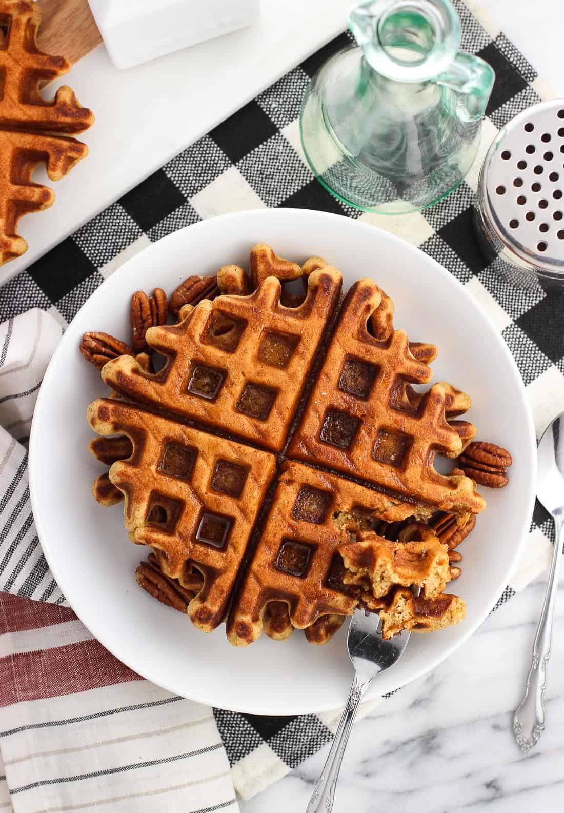 An overhead shot of two gingerbread waffles served on a plate with maple syrup and pecans