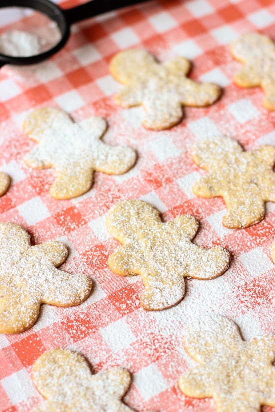 Thin person-shaped sugar cookies on a placemat dusted with powdered sugar.