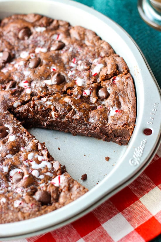 Sliced cookie cake in a metal cake pan with one wedge removed.