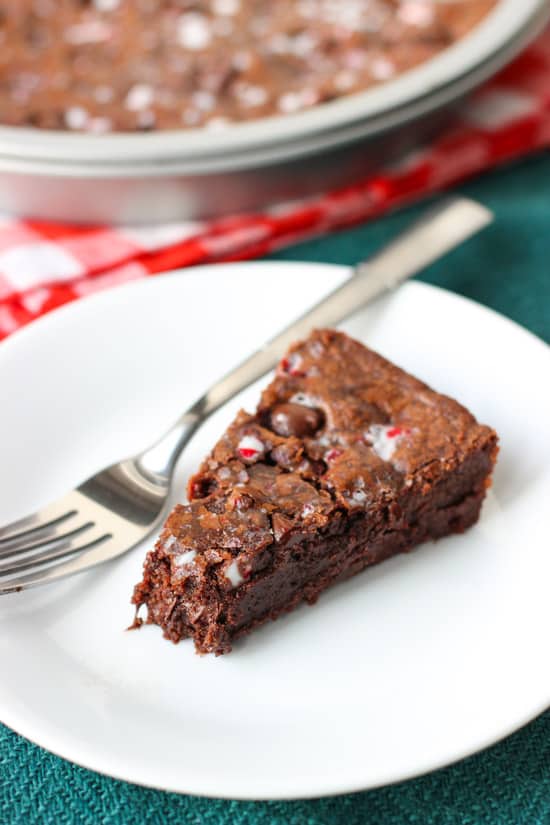 A slice of cookie cake on a plate with a fork and one bite removed.