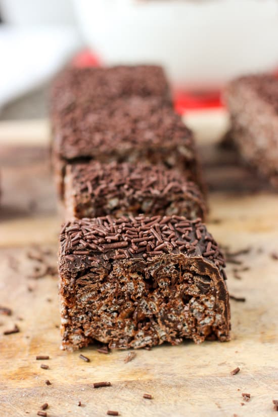 Lined up chocolate rice krispie treats on a wooden cutting board.