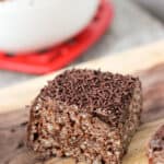 A wedge of chocolate rice krispie treats on a wooden board.