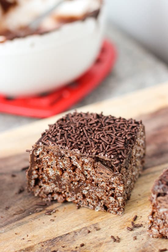 A corner piece of a chocolate rice krispie treat on a wooden board.
