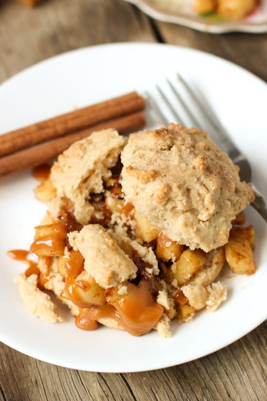 A slightly crumbed apple pie shortcake on a plate with a fork and cinnamon stick.