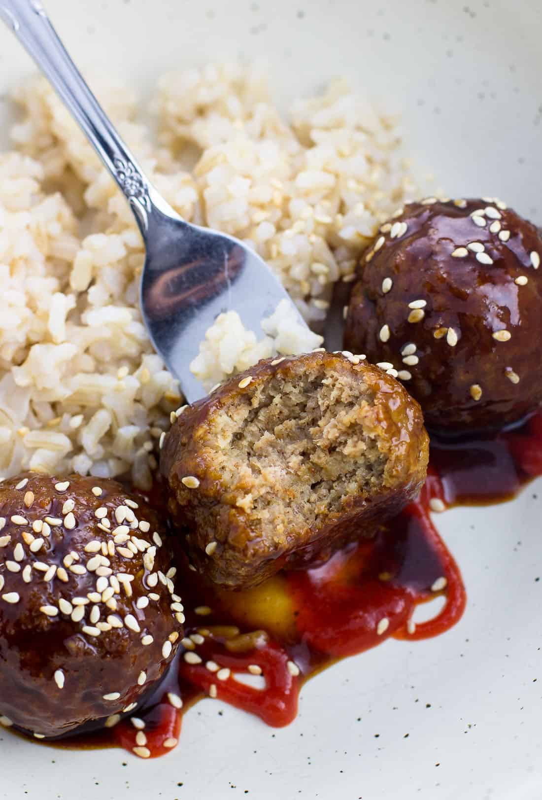 A close-up picture of a bite taken out of a meatball on a fork