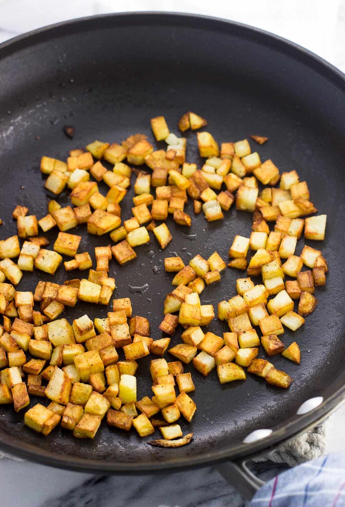 Small cubes of roasted potatoes in a skillet.