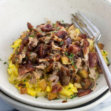 A pile of scrambled eggs, bacon, potatoes, pulled pork, and BBQ sauce in a bowl