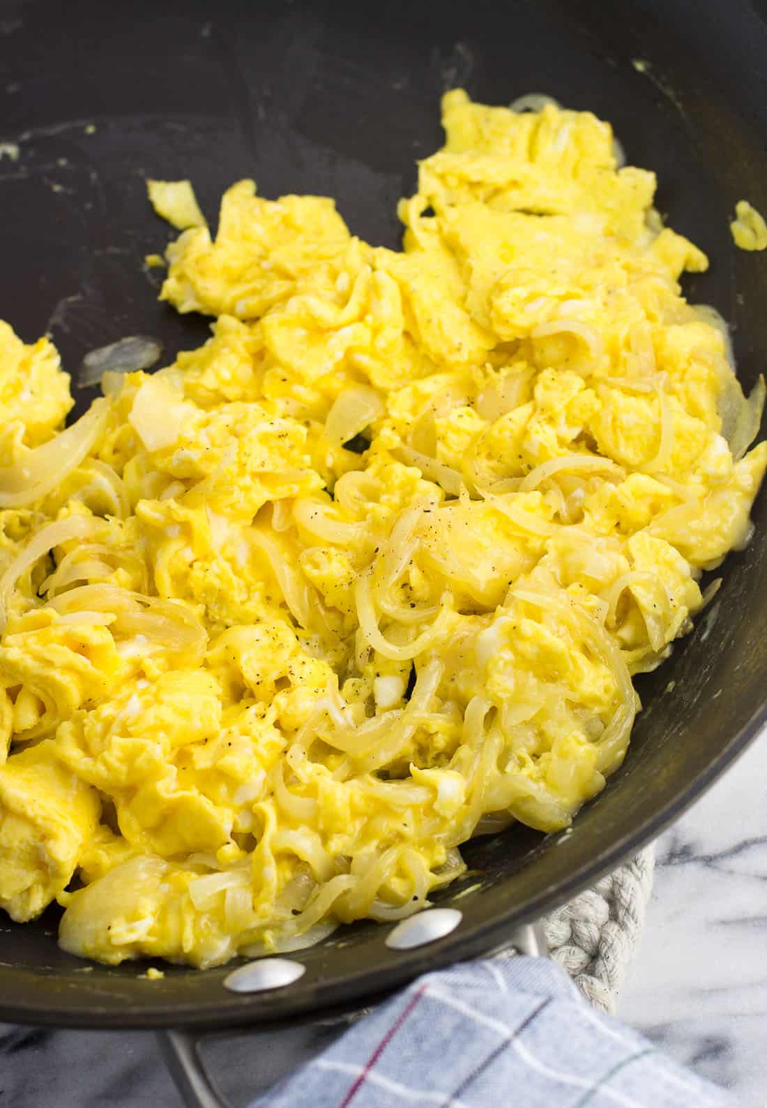 Scrambled eggs mixed with cheese and sauteed onion slices in a skillet.