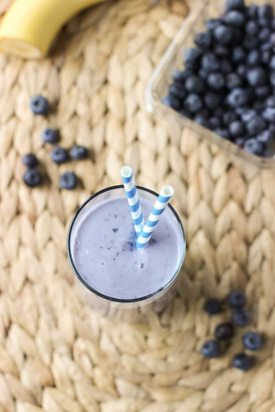 An overhead view of a smoothie with two paper straws surrounded by blueberries.