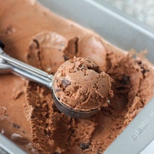 A mound of ice cream in a metal scoop resting in the ice cream container.