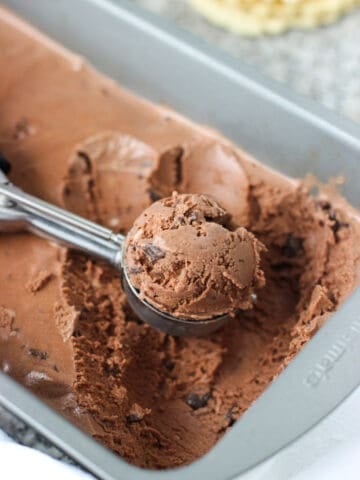 A mound of ice cream in a metal scoop resting in the ice cream container.