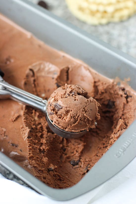 A mound of ice cream in a metal scoop resting in the ice cream container.