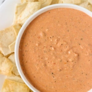 A bowl of dip on a plate of pita chips.