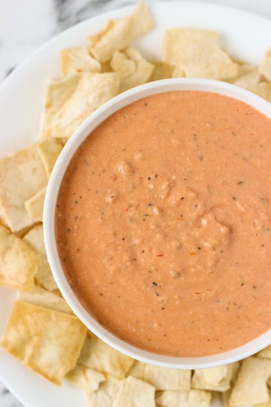 A bowl of dip on a plate of pita chips.