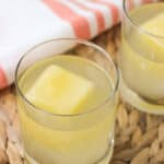 Two cocktails in small glasses with big pineapple ice cubes.
