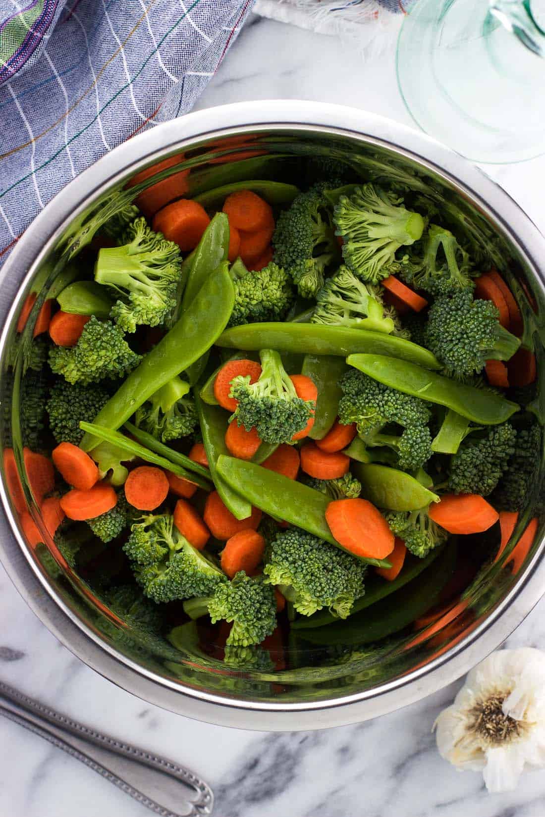 Raw broccoli florets, snow peas, and carrot slices in a mixing bowl.