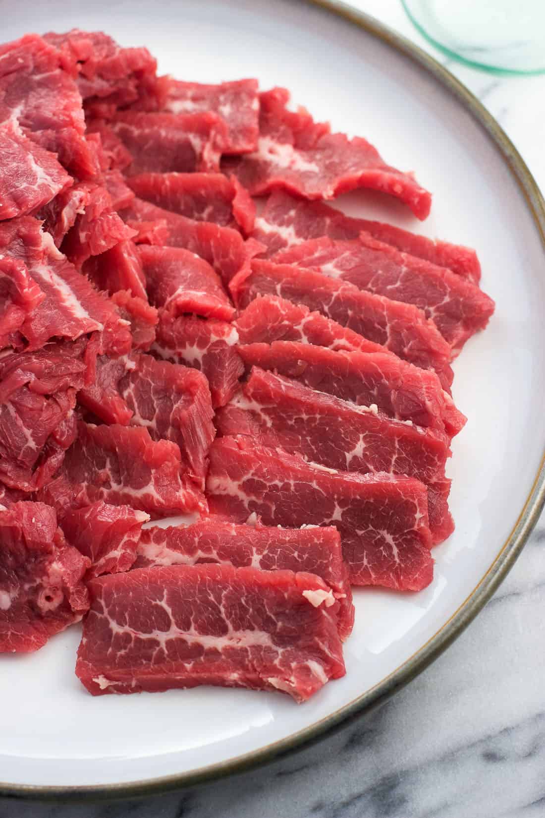 Raw strips of flank steak on a plate before being cooked.