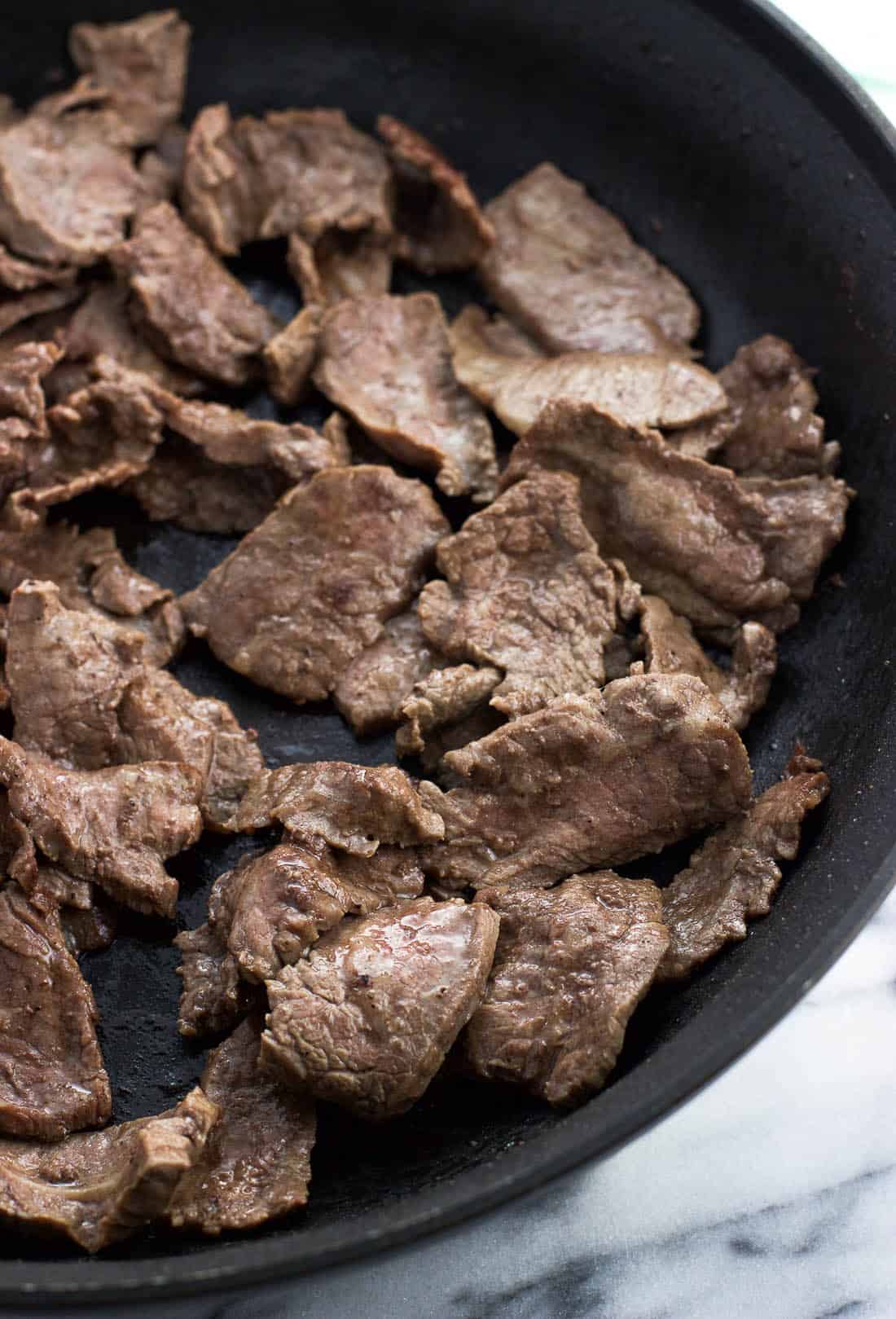 Cooked flank steak strips in a skillet