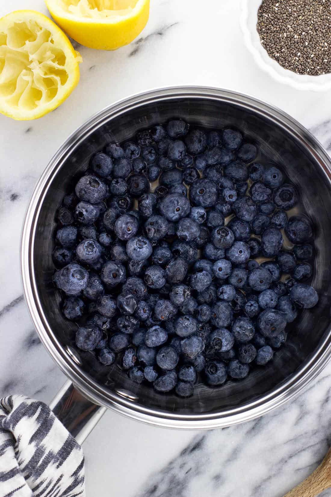 An overhead shot of a medium saucepan filled with fresh blueberries and lemon juice before heating