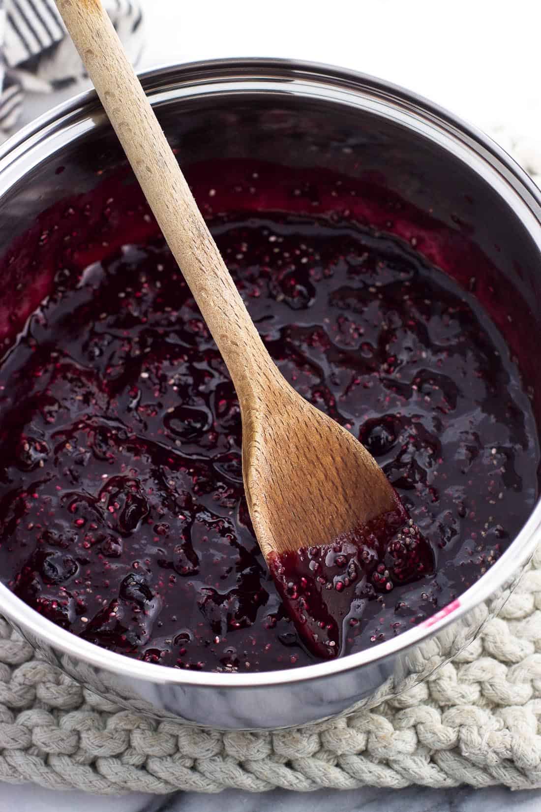 A wooden spoon in the saucepan of jam after stirring in the chia seeds