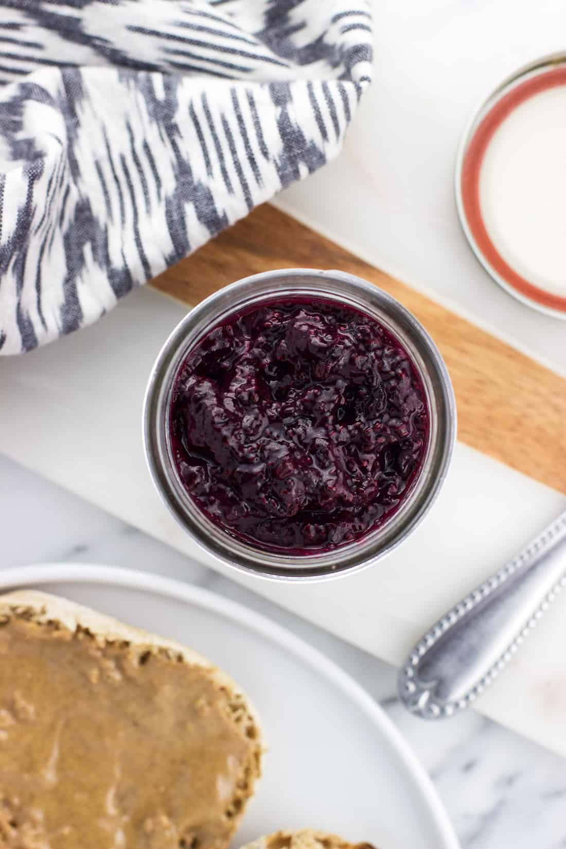 An overhead shot of a jar of jam next to a toasted english muffin