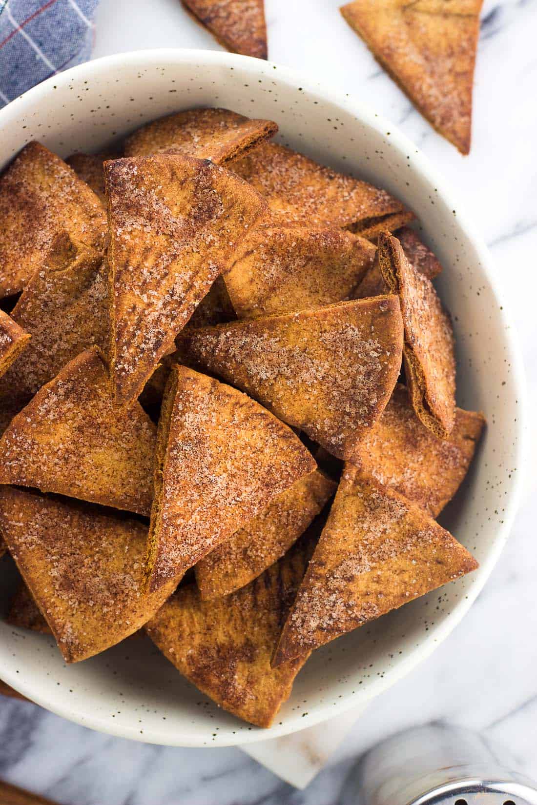An overhead shot of cinnamon sugar pita chips in a serving bowl on a marble board
