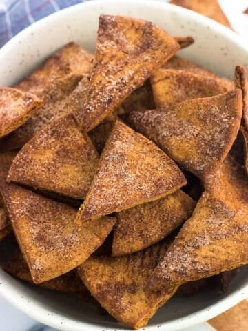 Cinnamon sugar pita chips in a ceramic bowl next to a dish towel