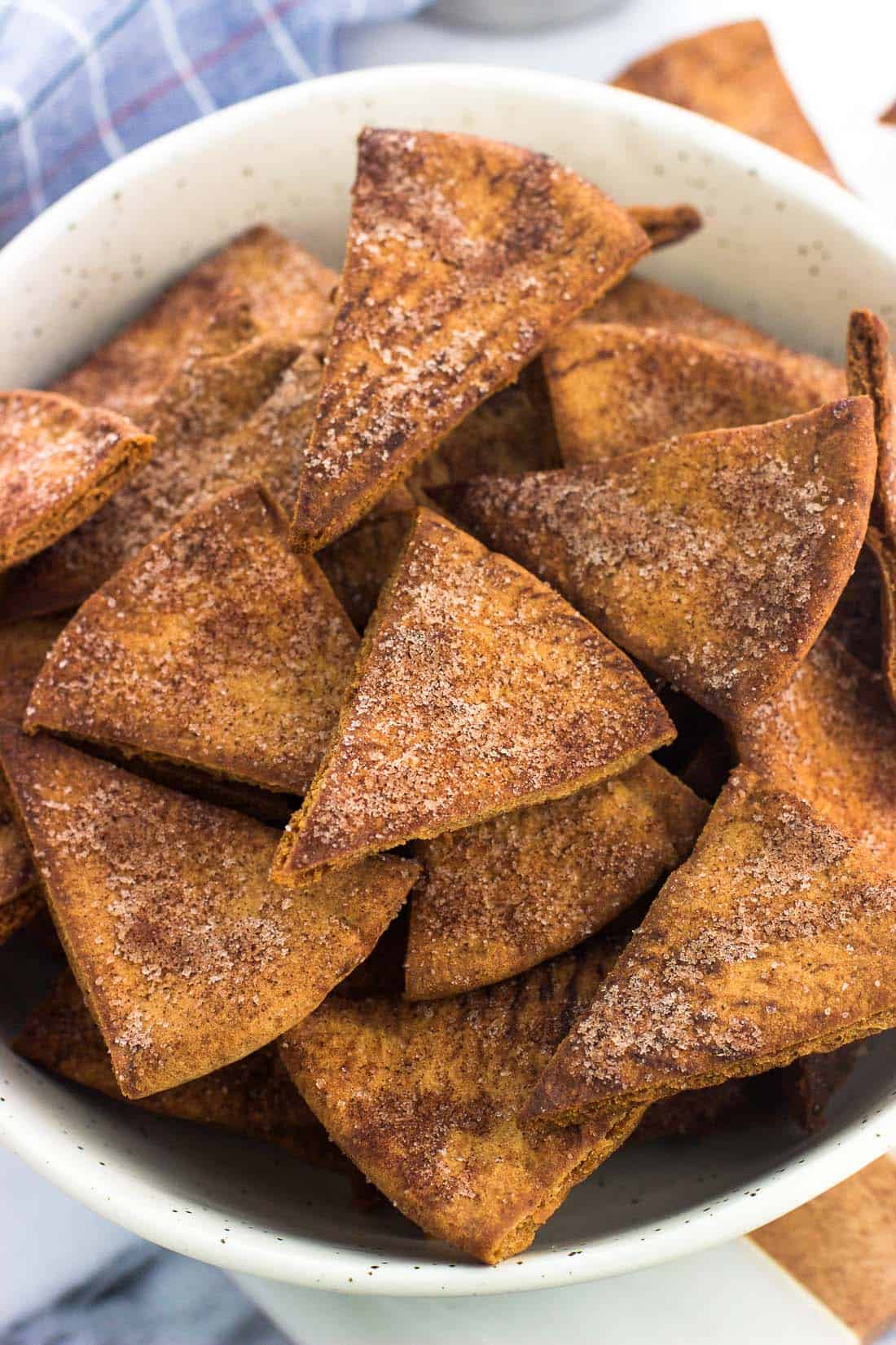 Cinnamon sugar pita chips in a ceramic bowl next to a dish towel