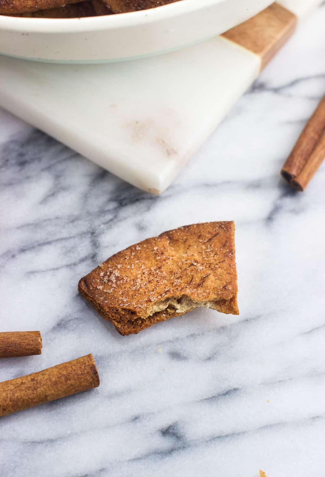 A crunchy pita chip on a marble board with a bite taken out of it