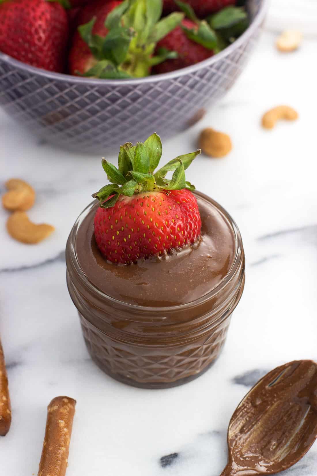A strawberry half dunked into a jar of chocolate cashew butter