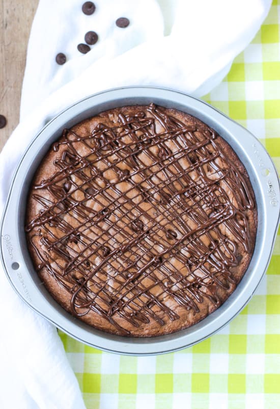 An overhead view of a chocolate-drizzled brownie cake in a metal cake pan.