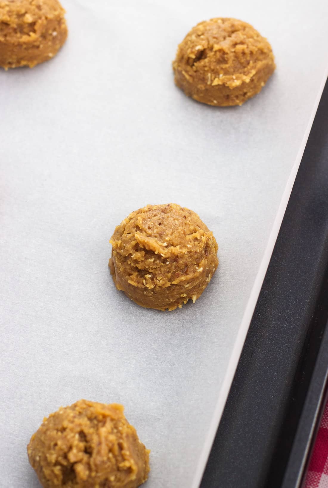 Raw cookie dough balls scooped onto a parchment-lined baking sheet.