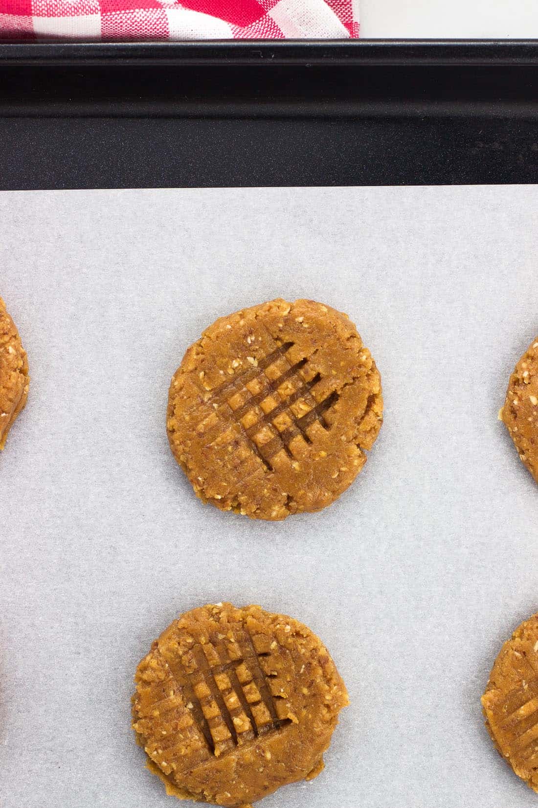 Flatted cookies on a baking sheet with a criss-cross pattern pressed on top.