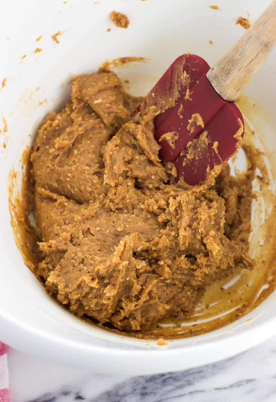 Peanut butter cookie dough in a mixing bowl with a spatula.