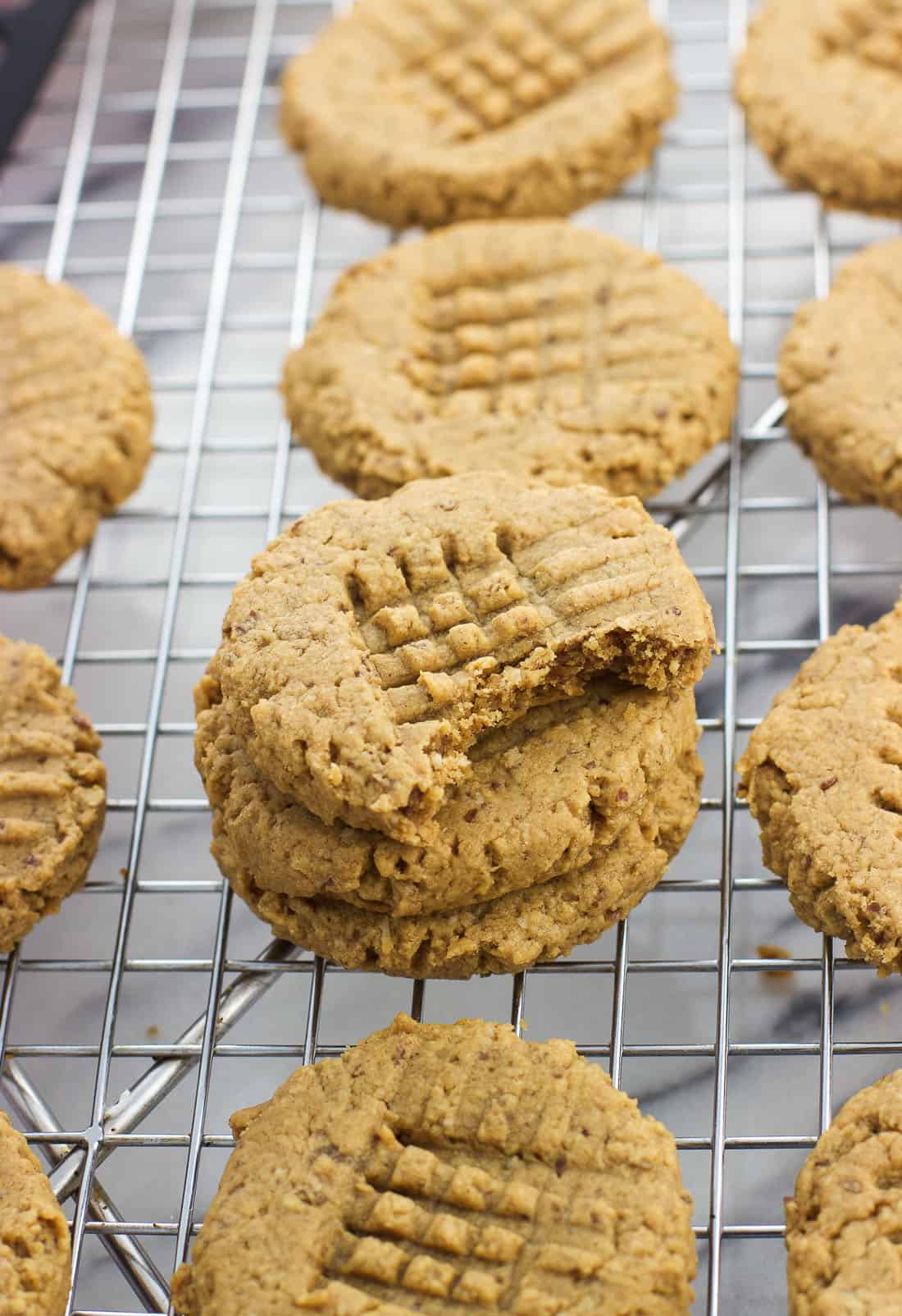 A stack of peanut butter cookies on a wire rack with a bite taken out of the top cookie.