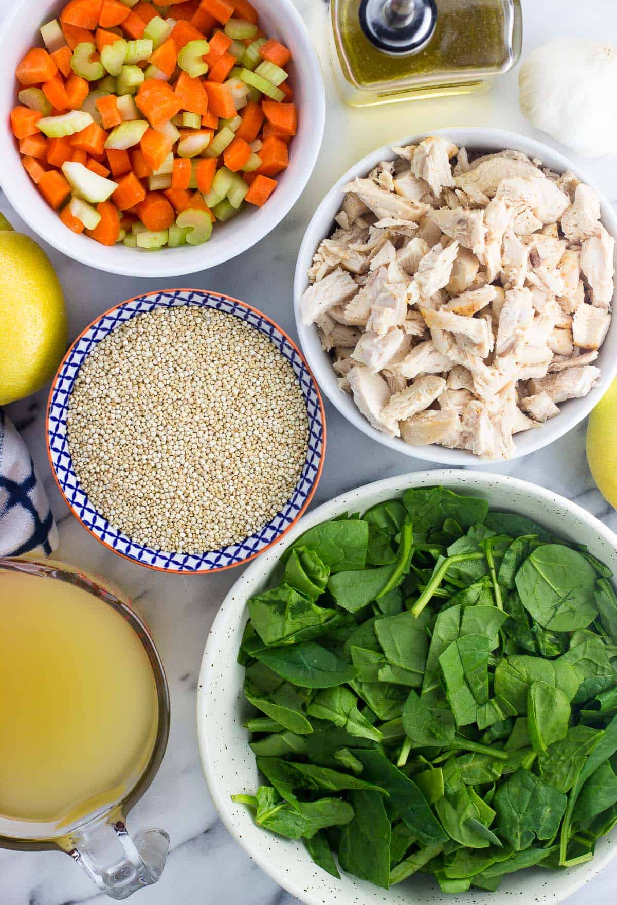 Soup ingredients like spinach, chicken, quinoa, etc. in separate ceramic bowls on a marble board.