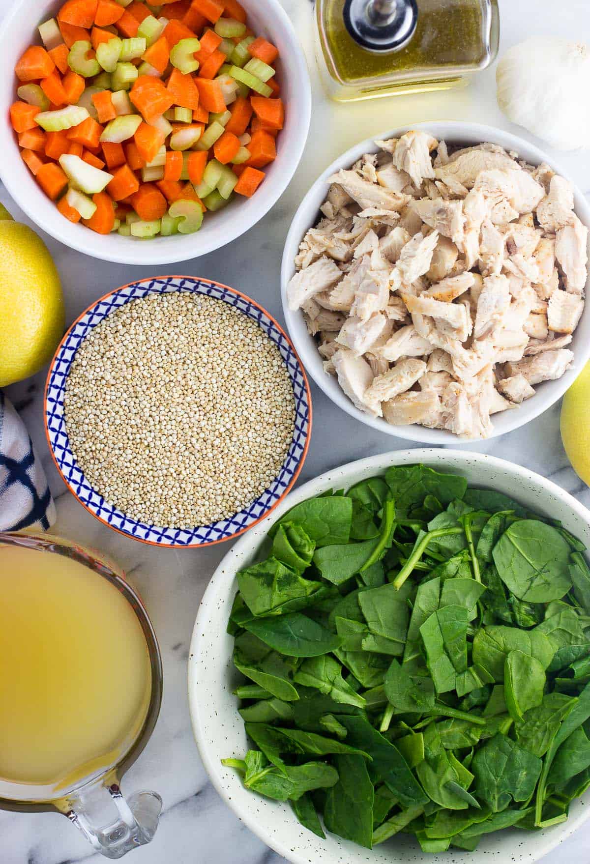 Soup ingredients like spinach, chicken, quinoa, etc. in separate ceramic bowls on a marble board