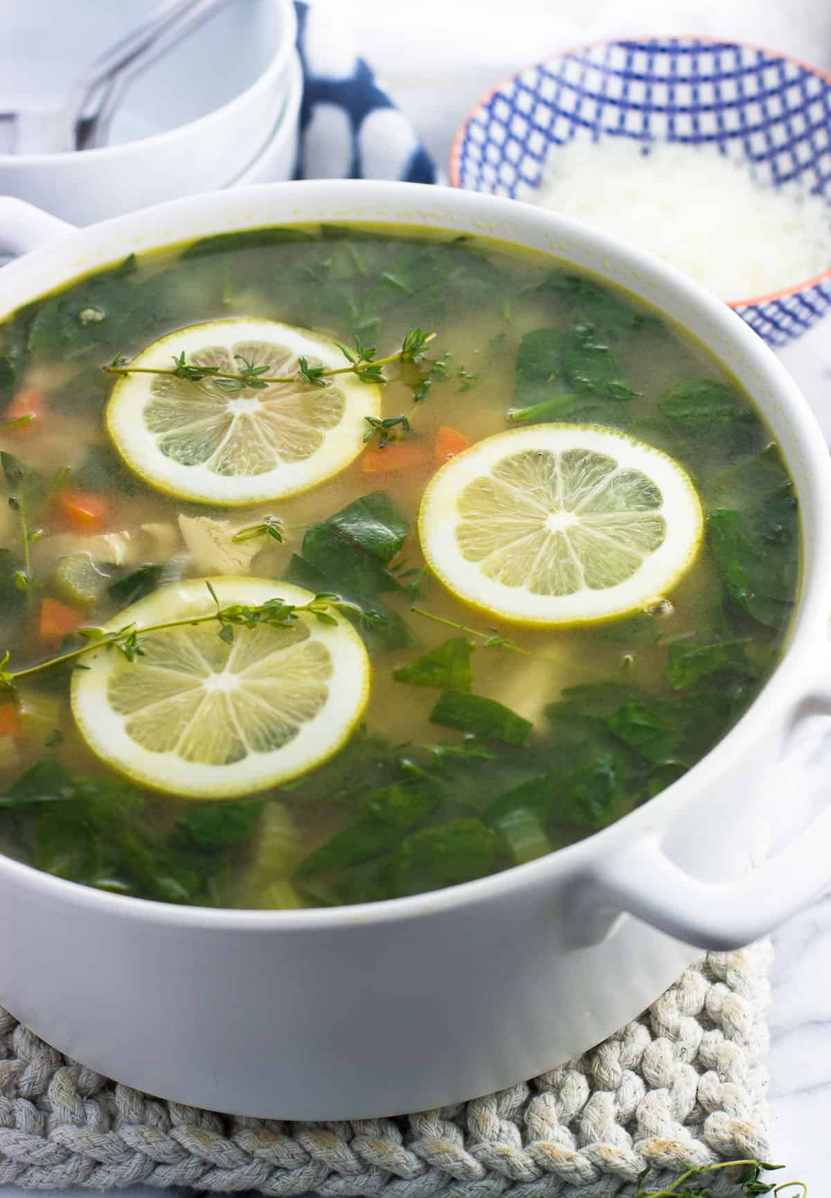 A big ceramic soup pot filled with soup and garnished with three lemon rounds.