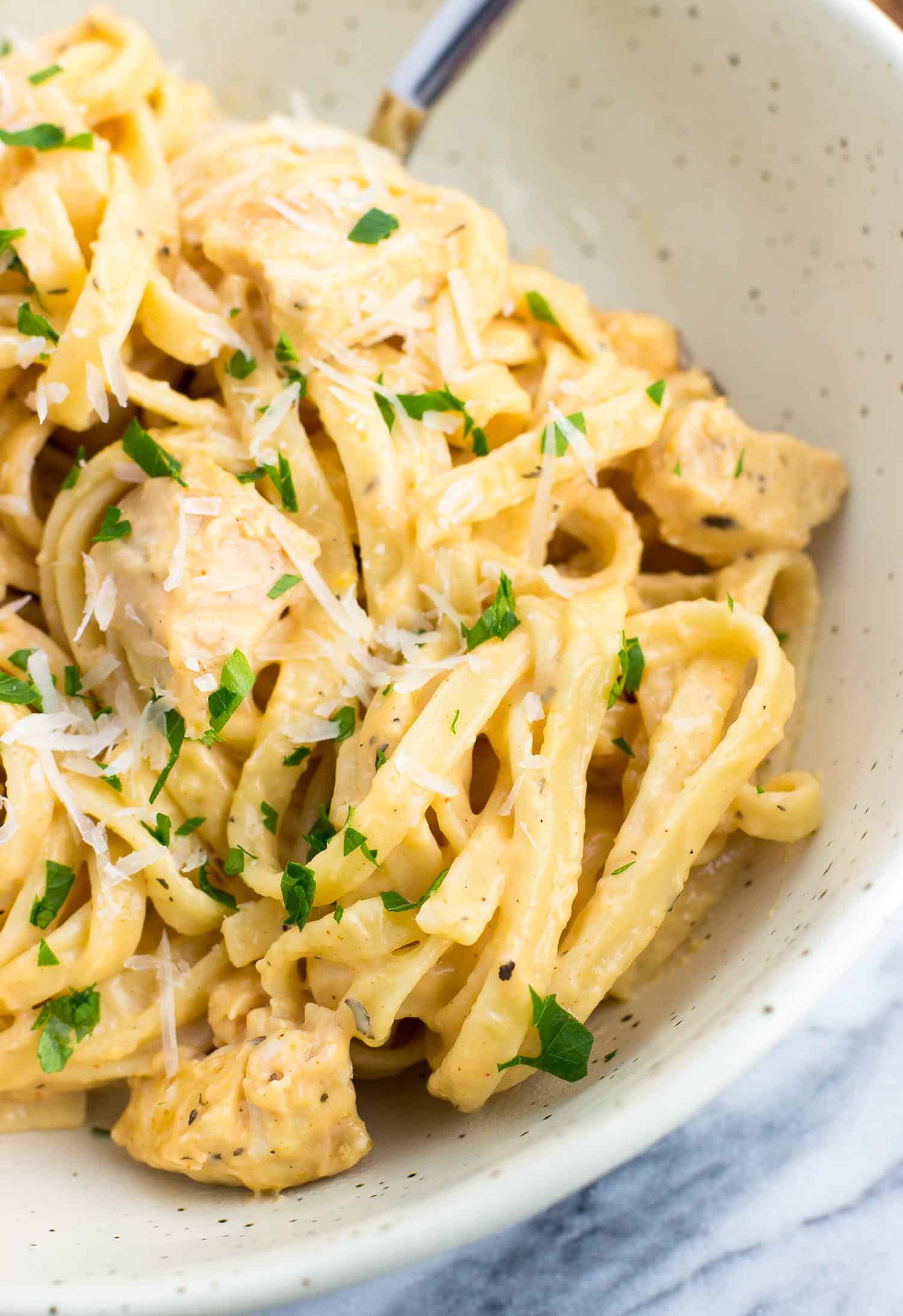 A close-up shot of buffalo chicken alfredo sauce on fettuccine in a bowl with a fork.