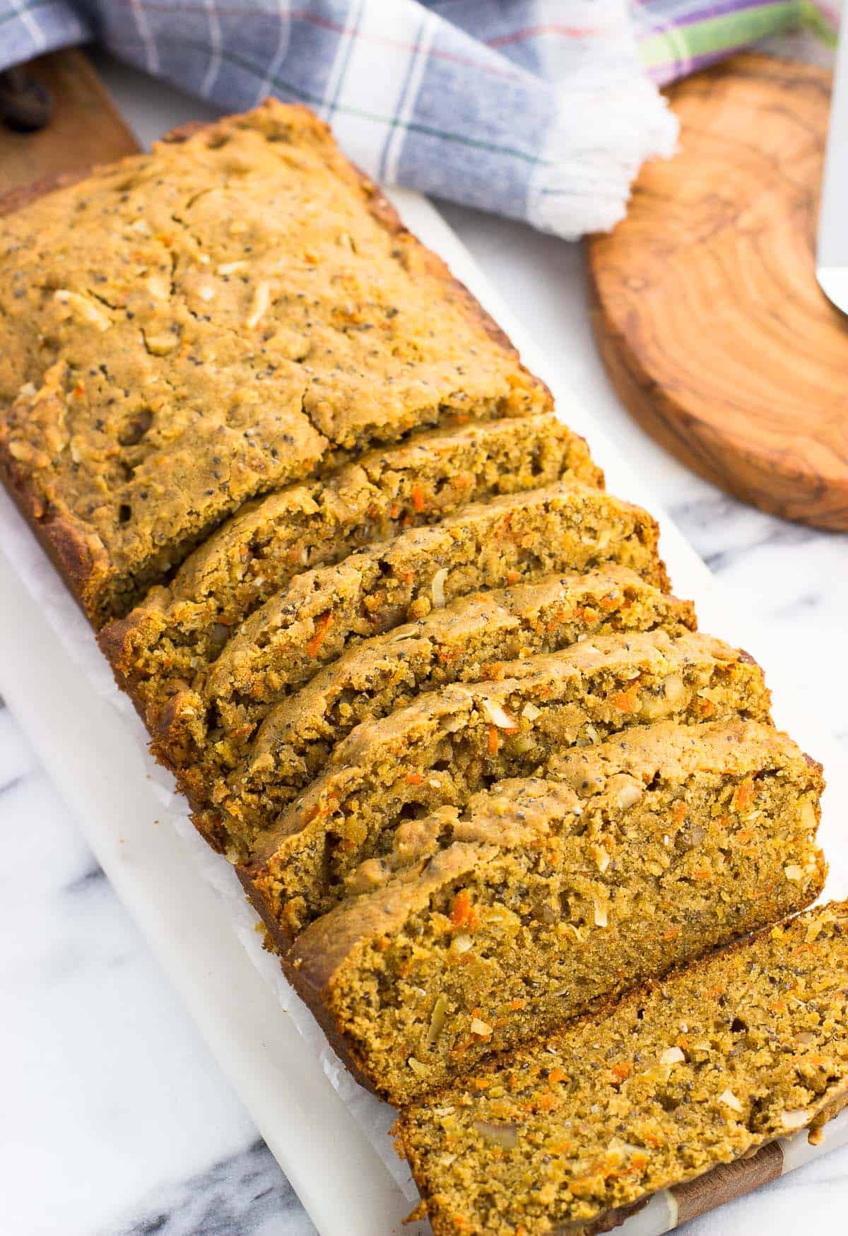 A partially sliced loaf of morning glory bread on a marble serving board.